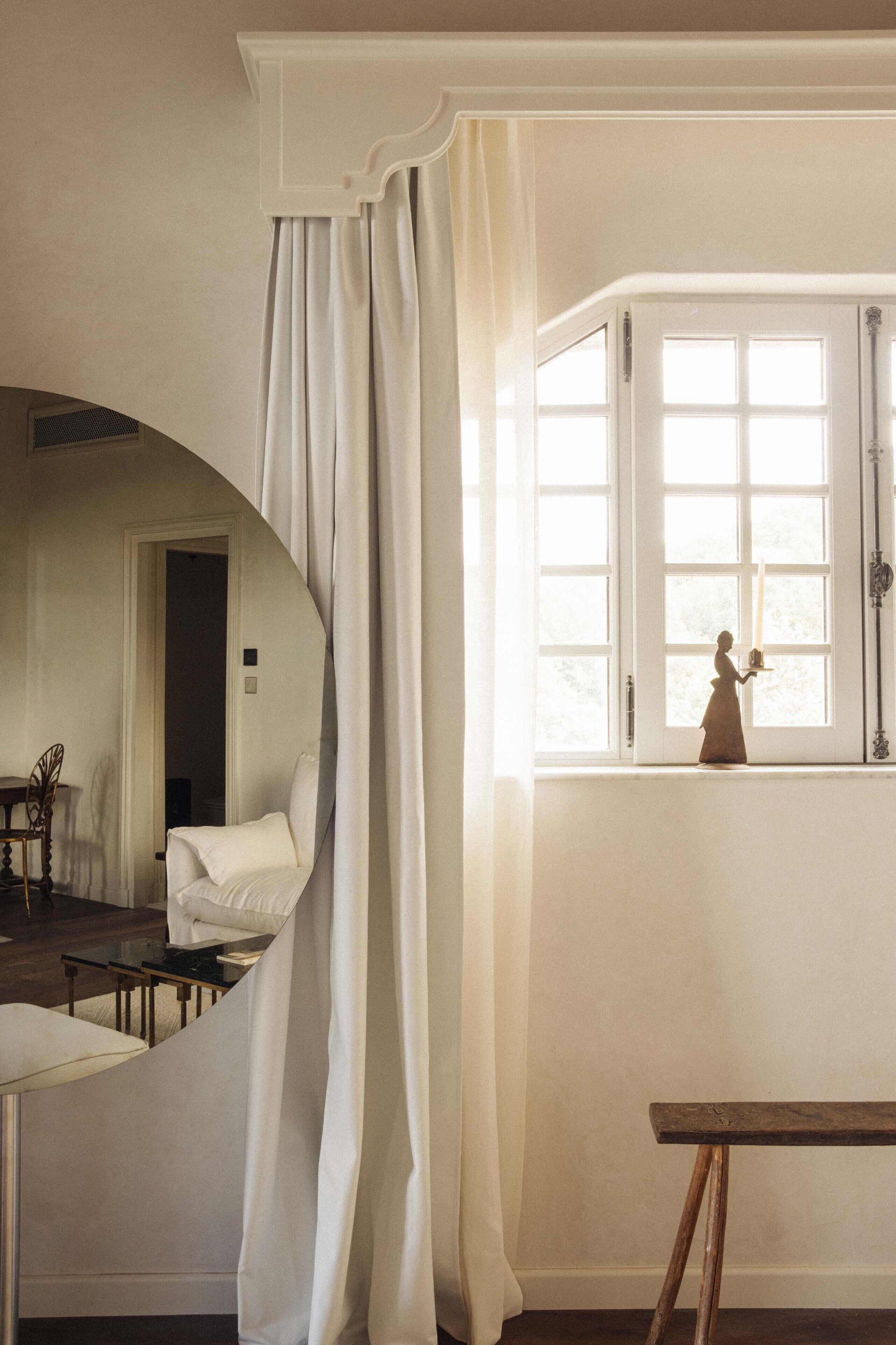 A room with a large window, a wooden table, and a mirror reflecting part of the room.