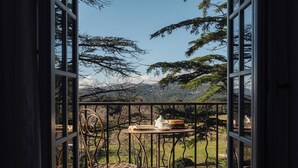 An open balcony with a wrought iron chair and table, overlooking a mountainous landscape.
