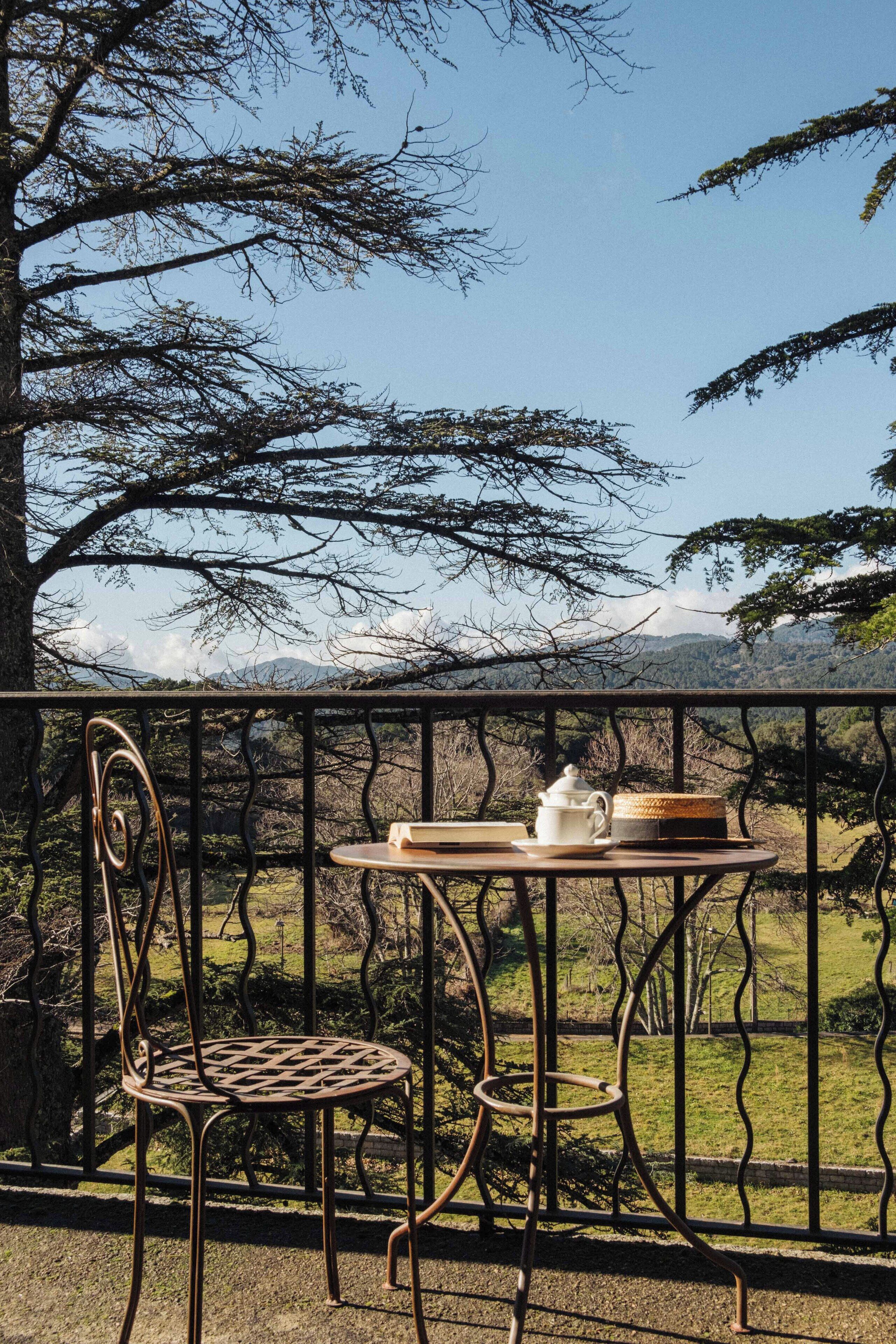A balcony with a table and chair, a teapot, and a tray, overlooking a mountainous landscape.