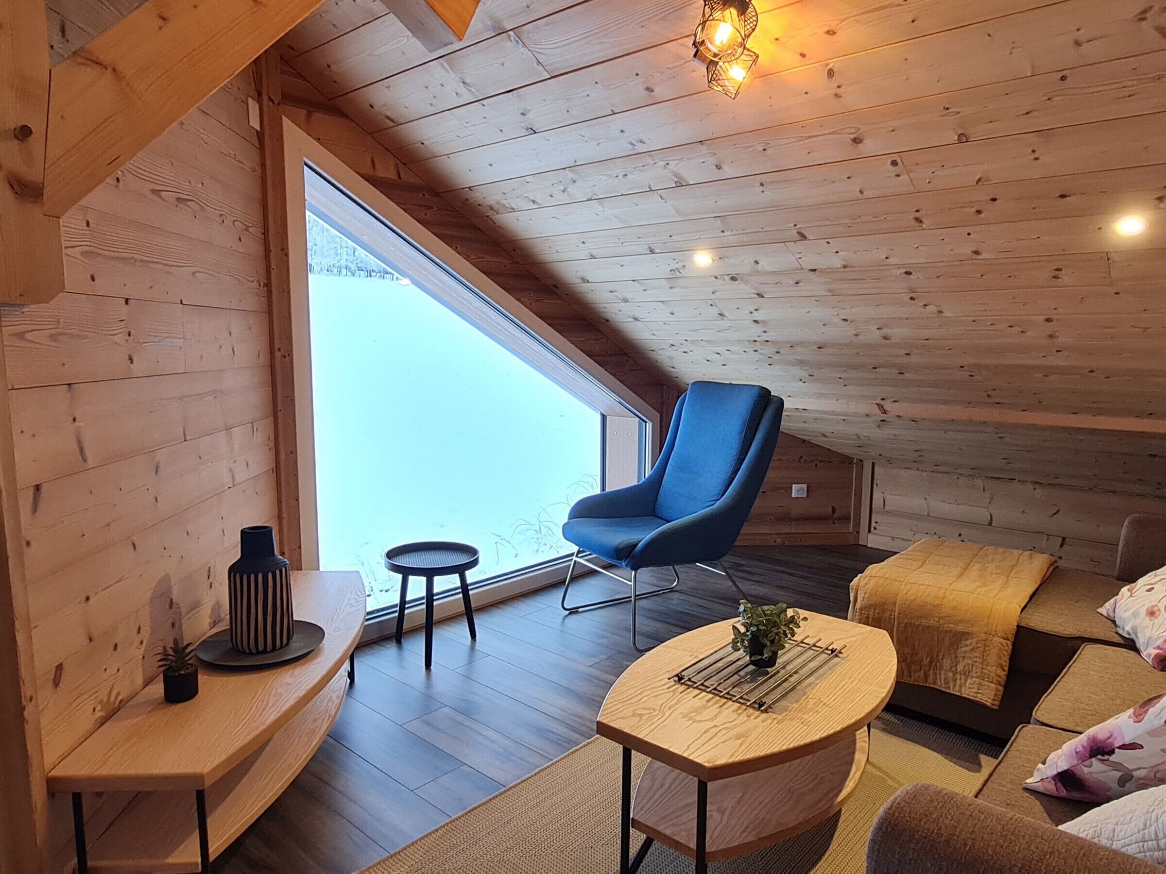 A cozy wooden room with a blue chair, a small round table, and a sofa.