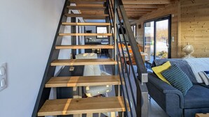 A wooden staircase with a black railing leading to a room with a sofa and a window. - Nature Chalet with Sauna and WIFI near Gérardmer (Anould)