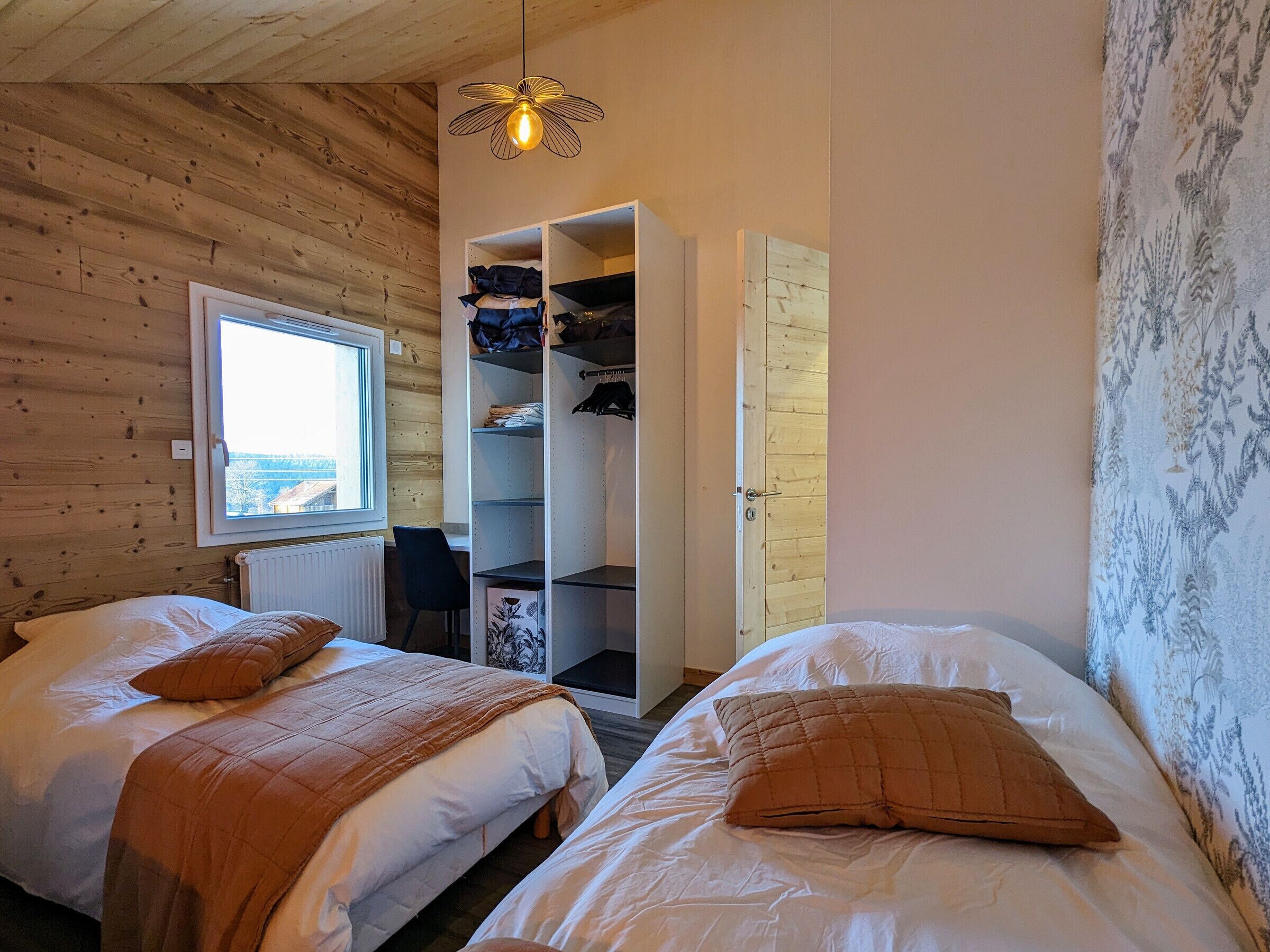 Una habitación con dos camas, una ventana, un armario y una lámpara colgante.