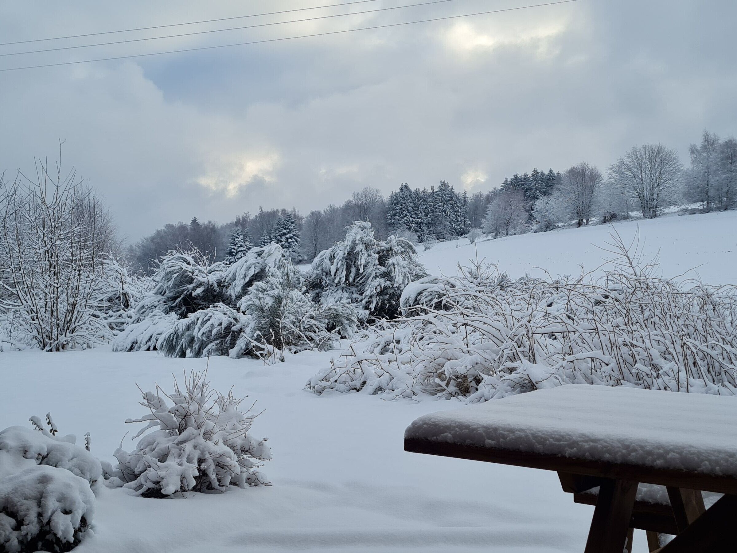 A snowy landscape with a wooden bench in the foreground.
