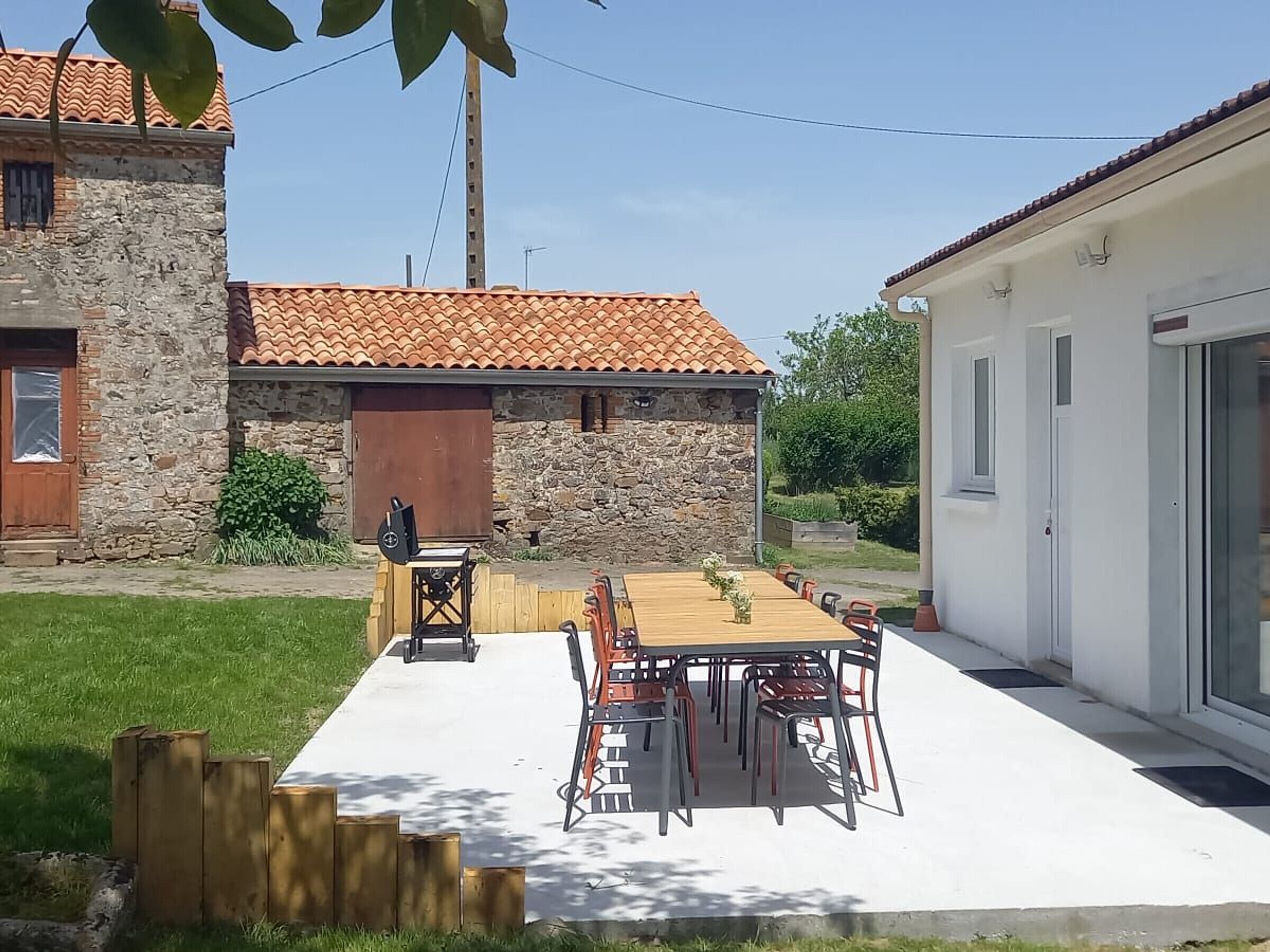Eine Terrasse mit Tisch und Stühlen, ein Steinhaus mit Ziegeldach und ein weißes Gebäude mit Glastür.