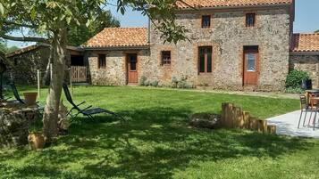 A stone building with a tiled roof, a grassy yard, and a wooden fence.