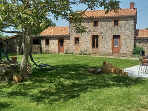 Un edificio de piedra con techo de tejas, patio cubierto de césped y valla de madera.