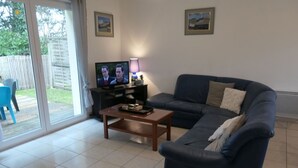 A living room with a dark blue sofa, a wooden coffee table, a TV on a stand, and a lamp. There are two framed pictures on the wall. - House in Sarzeau, 3 bedrooms, near beach and shops, pets allowed, internet (Sarzeau)