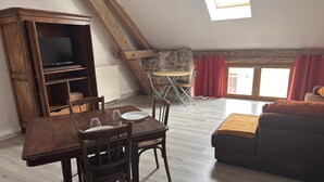 A loft-style room with a dining table, chairs, a sofa, a TV, and a stone wall. - Countryside Cottage with Wifi and Pets Allowed (Saint-Bonnet-de-Four)