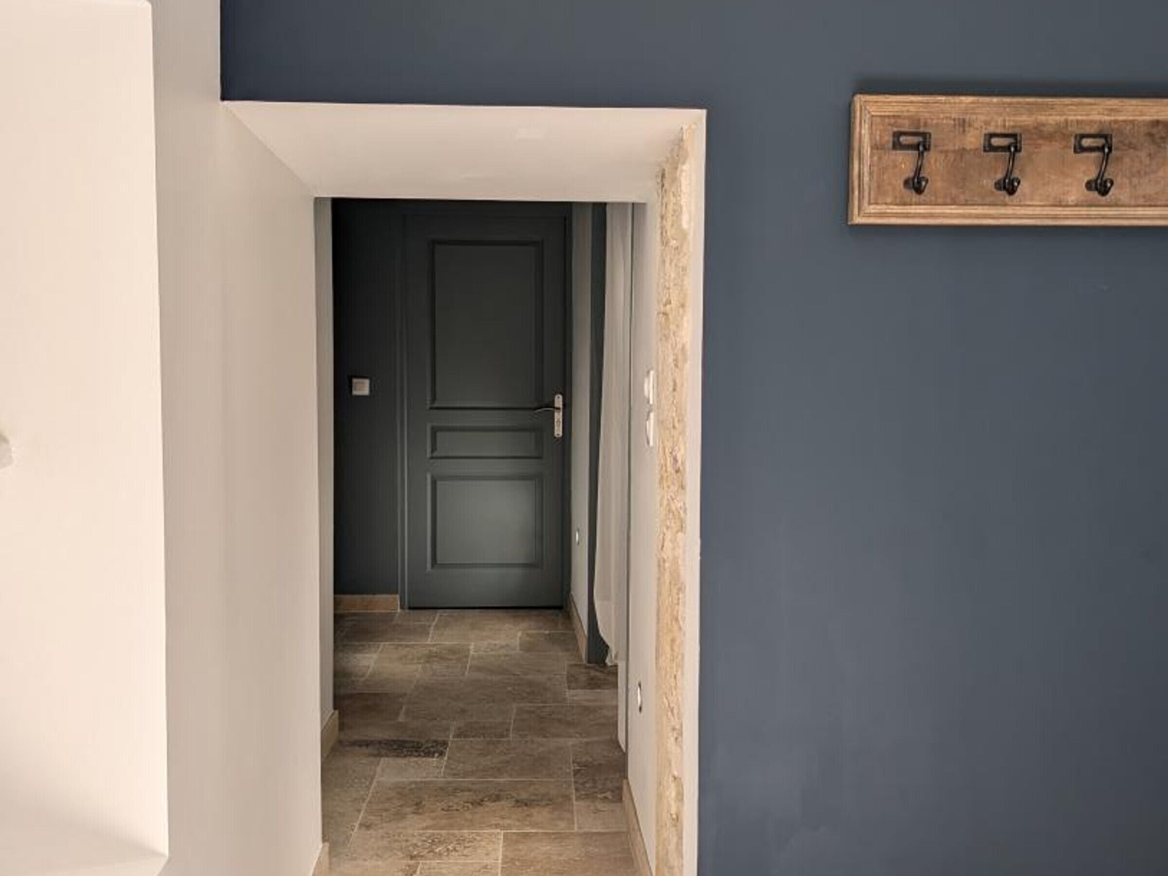 A hallway with a dark door, a wooden coat rack, and a tiled floor.