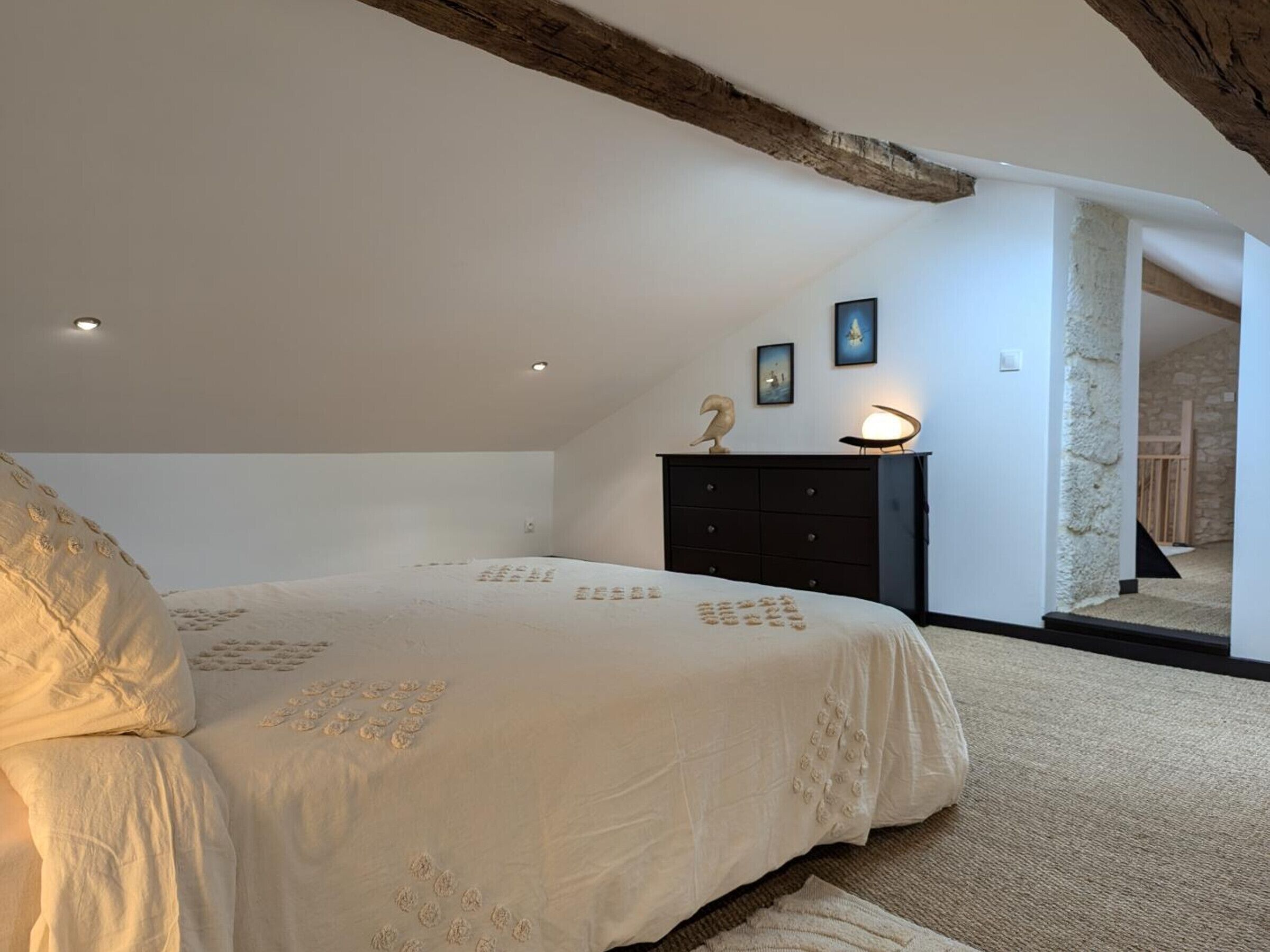 A bedroom with a large bed, a dresser, and a stone wall.
