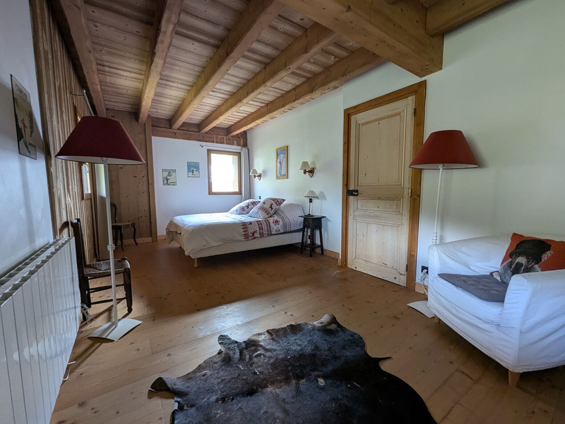 Ein Zimmer mit einem Bett, einem weißen Sofa, einer Lampe, einer Tür und einem großen Tierfell auf dem Boden.
