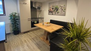 A modern kitchen with white cabinets, a wooden dining table, and a black sofa.