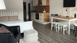 A modern kitchen with white cabinets, a wooden countertop, and a built-in oven. There is a dining area with a white table and chairs. - Renovated loft with parking space and balcony (Lörrach)