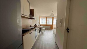 A narrow hallway leading to a dining area with a window, a kitchen with a stove, and a door with a phone. - Renovated loft with parking space and balcony (Lörrach)
