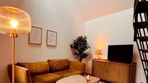 A modern living room with a sofa, a coffee table, a floor lamp, a TV, and a staircase. - La Maison de Victoire et Alix - house with garden in the heart of Pontrieux (Pontrieux)