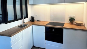 A modern kitchen with white cabinets, a wooden countertop, a black dishwasher, and a window with frosted glass. - La Maison de Victoire et Alix - house with garden in the heart of Pontrieux (Pontrieux)