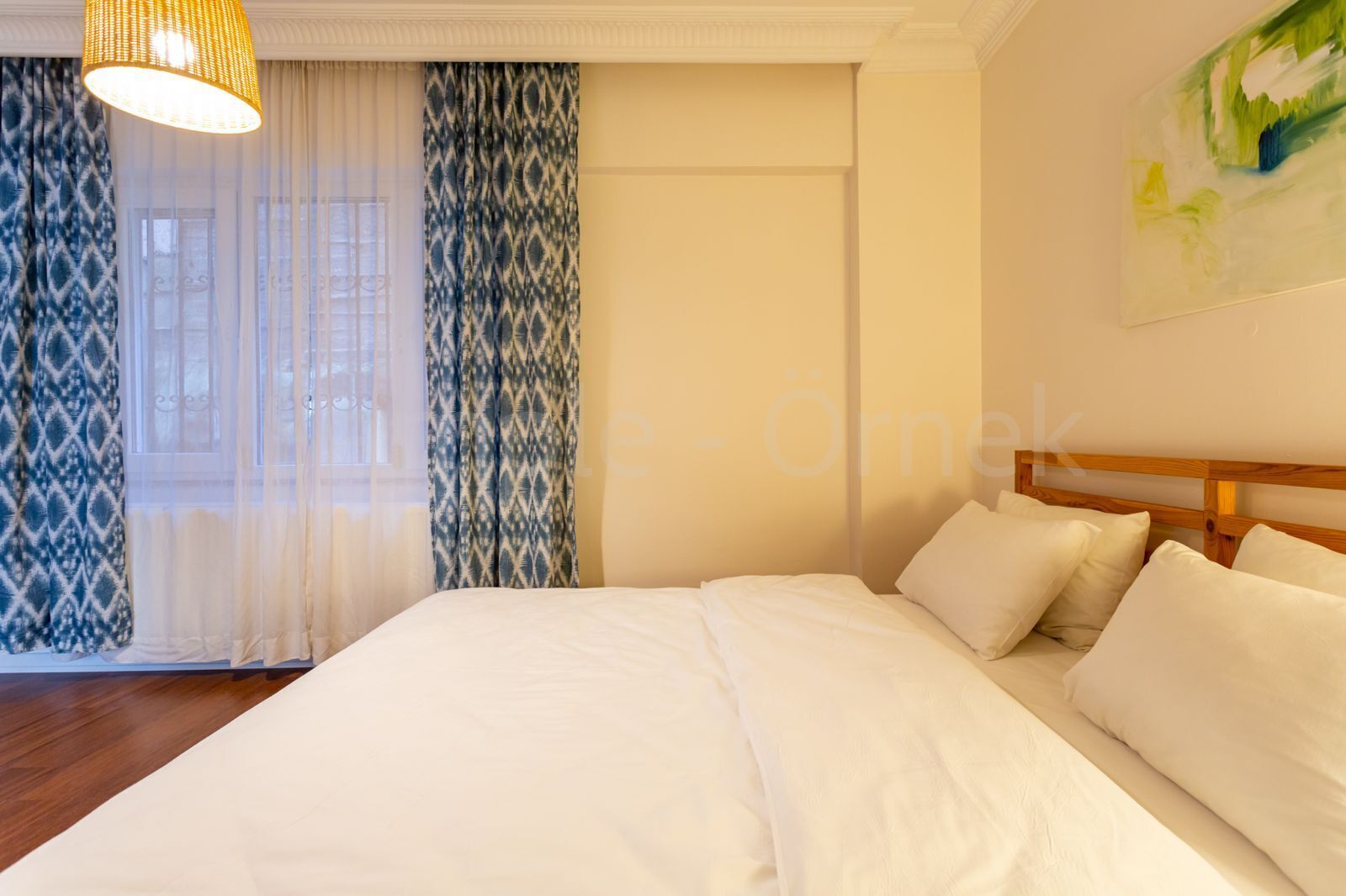A bedroom with a large bed, a wooden headboard, and a window with patterned curtains.