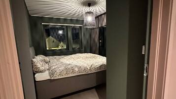 A modern bedroom with a bed, a hanging light fixture, and a window.