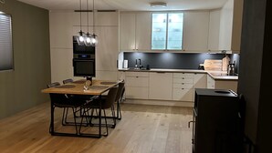 A modern kitchen with white cabinets, a wooden dining table, and a black refrigerator. - Kvaloysletta - 2 Bed Apartment - Free Parking (Tromsø)