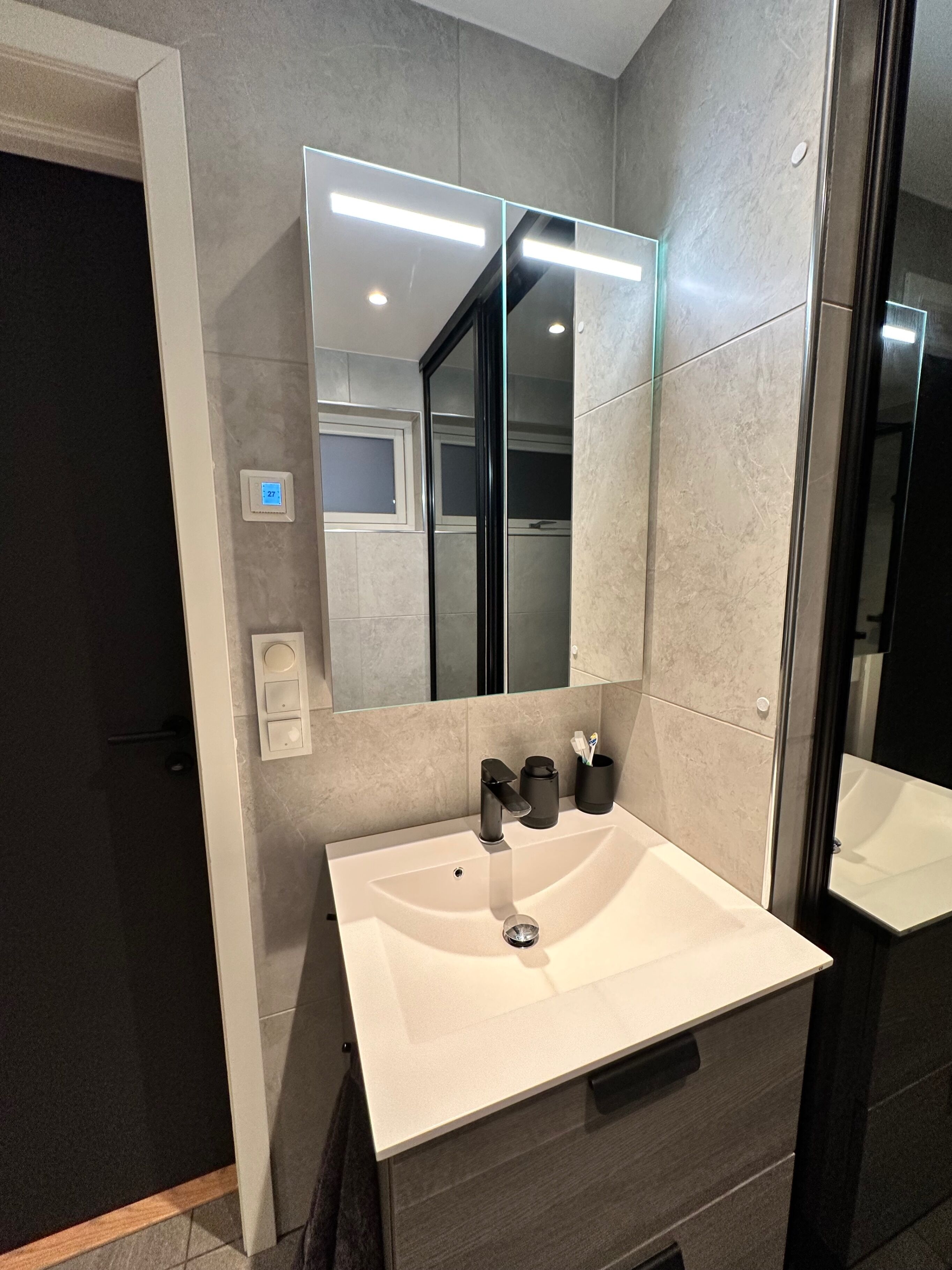 A modern bathroom with a large mirror, a white sink, and a dark-toned vanity.