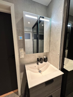 A modern bathroom with a large mirror, a white sink, and a dark-toned vanity. - Kvaloysletta - 2 Bed Apartment - Free Parking (Tromsø)