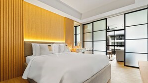 Habitación de hotel moderna con una cama grande, paneles de madera y vistas de la ciudad a través de ventanales del suelo al techo.