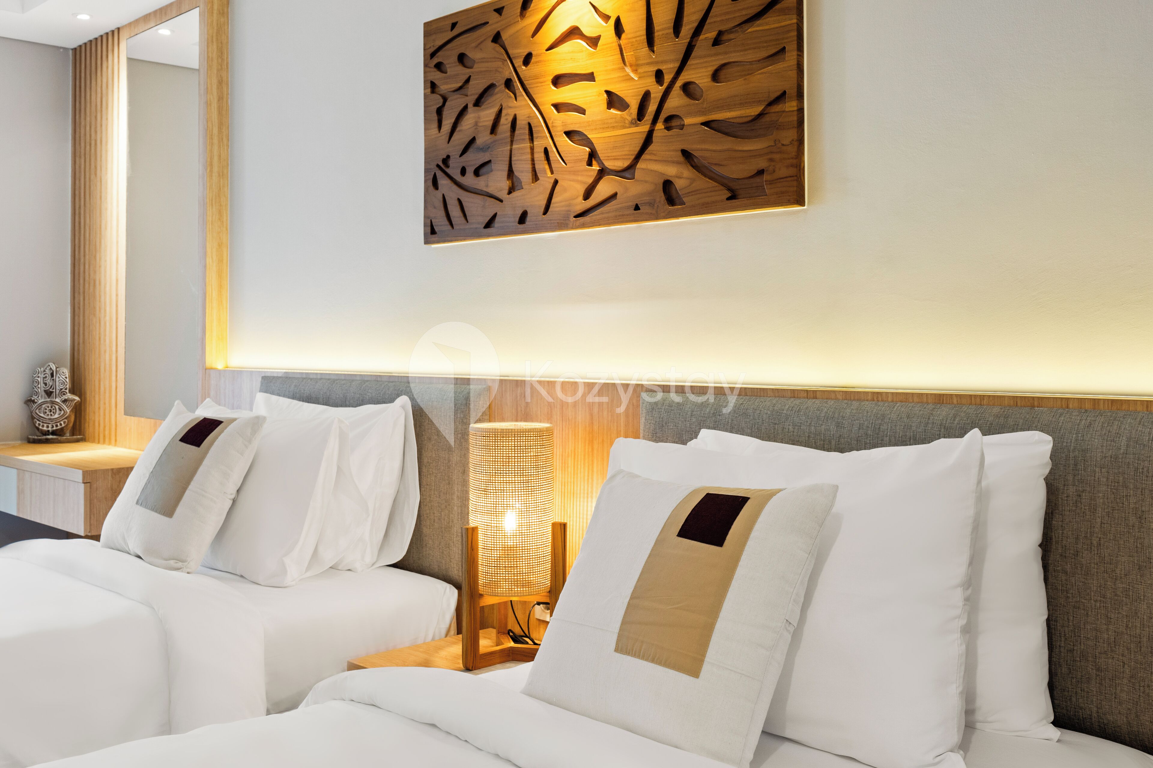 A modern hotel room with a large bed, a bedside table with a lamp, and a decorative wall piece.