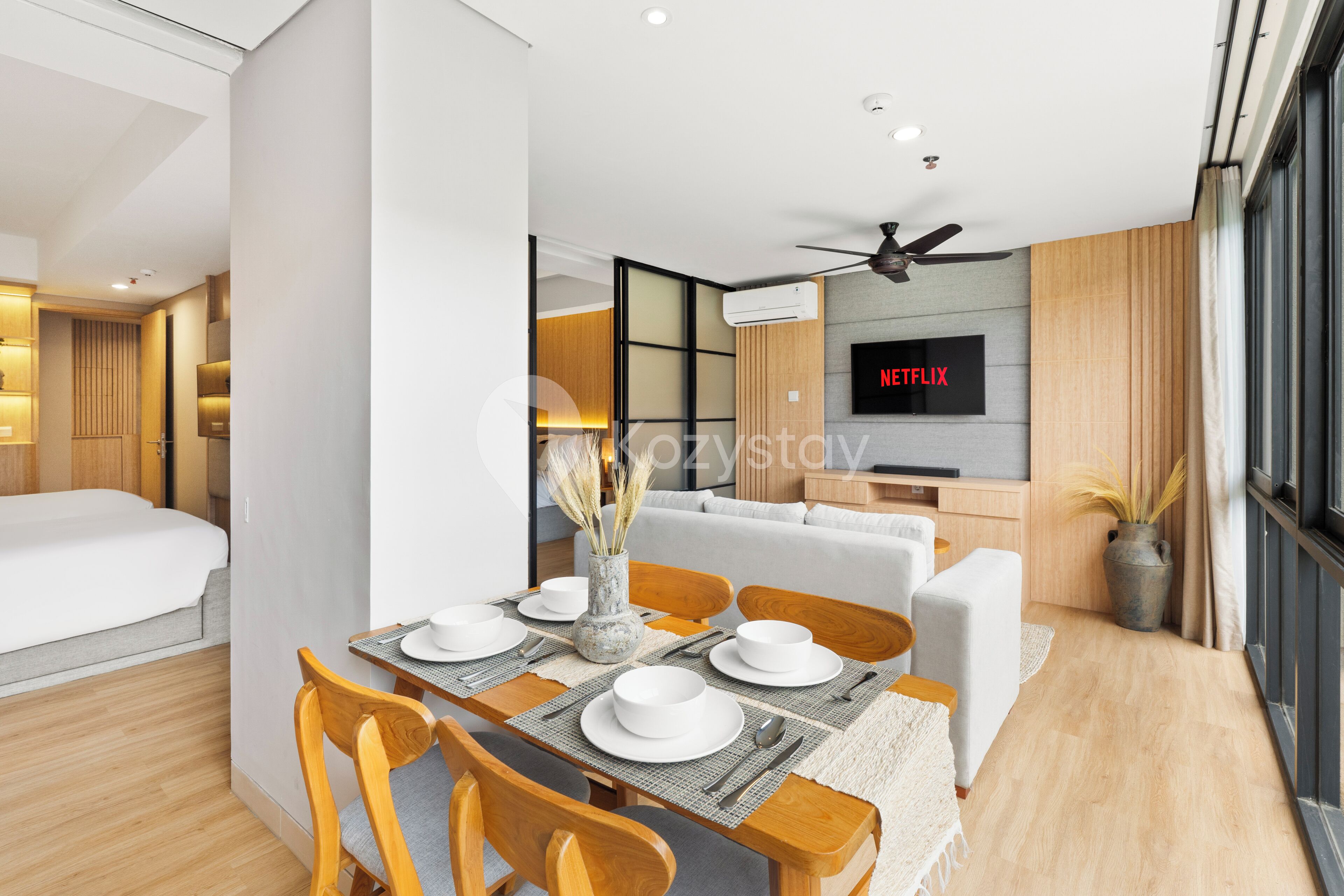 Una habitación de hotel moderna con comedor, sofá, televisor y ventilador de techo.