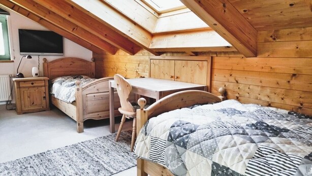 A cozy attic bedroom with a wooden sloped ceiling, a bed, a desk, and a chair. - Fewo "bei Tannenbaums", Oberstaufen (Oberstaufen)