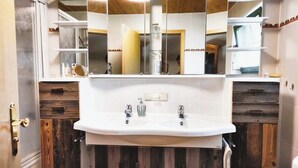 A bathroom with a white sink, two faucets, and a mirror above it. There are wooden cabinets below the sink and a door with a brass handle to the left. - Fewo "bei Tannenbaums", Oberstaufen (Oberstaufen)