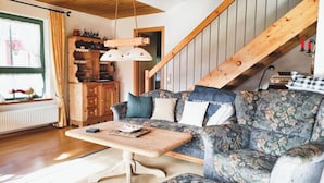 A cozy living room with a wooden staircase, a sofa with floral upholstery, and a wooden coffee table. - Fewo "bei Tannenbaums", Oberstaufen (Oberstaufen)