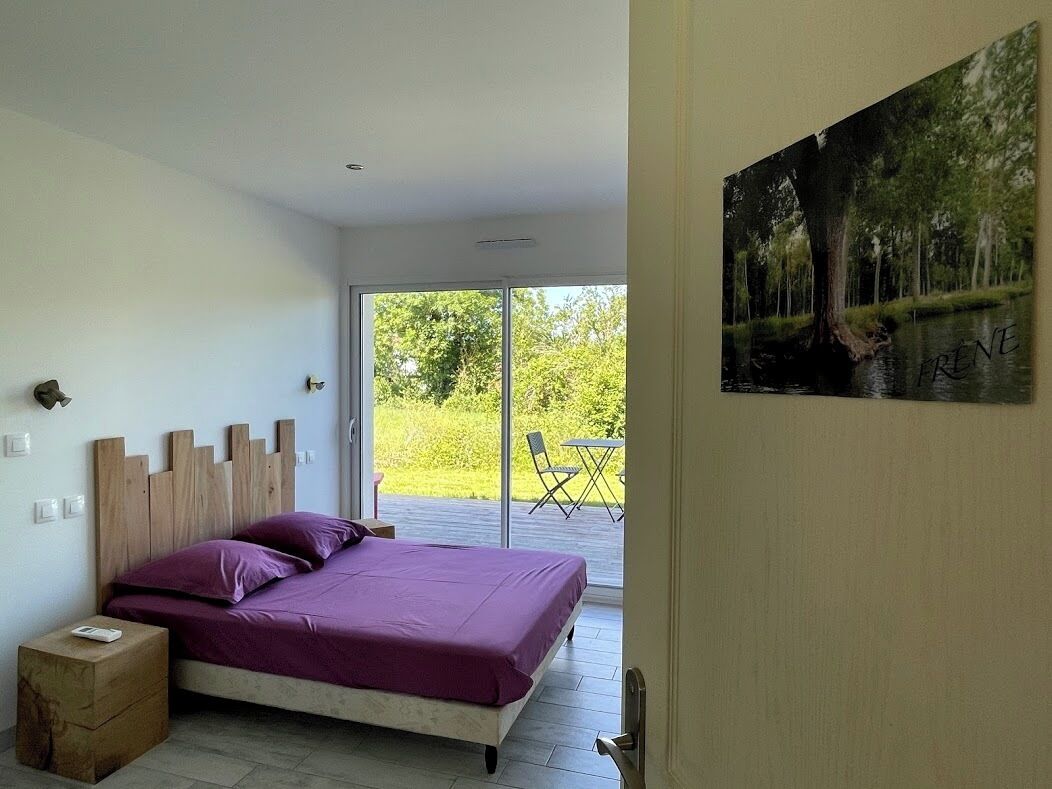 Un dormitorio con cama, cabecera de madera y vista a un balcón con mobiliario exterior.