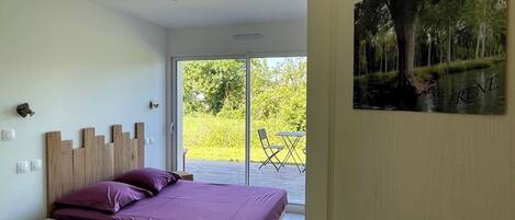 Un dormitorio con cama, cabecera de madera y vista a un balcón con mobiliario exterior.