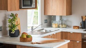Una cocina moderna con armarios de madera, un microondas integrado, un lavamanos y una encimera con tabla de cortar y frutero.