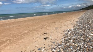 Una playa de piedras y arena, cielo despejado y el océano al fondo.