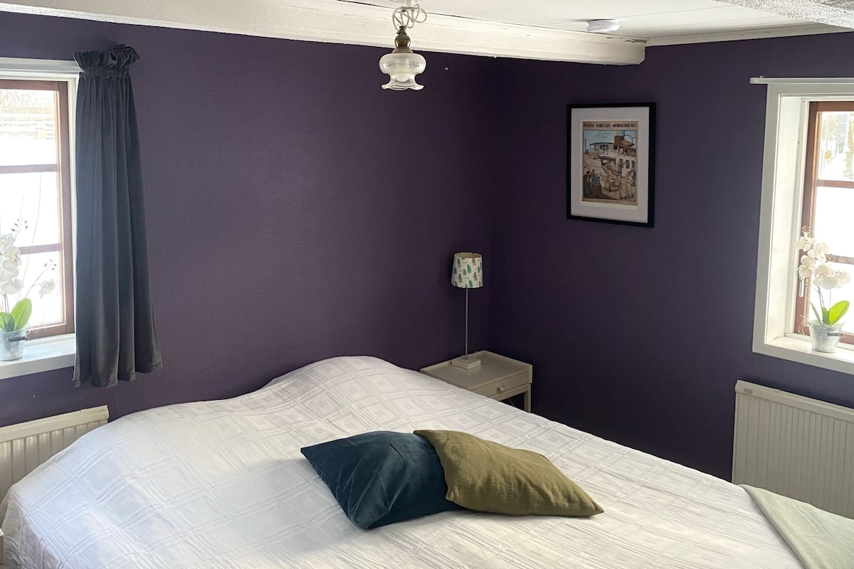 A bedroom with a bed, a nightstand, a lamp, a window with curtains, and a poster on the wall.