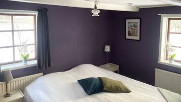 Een slaapkamer met een bed, nachtkastje, lamp, raam met gordijnen en een poster aan de muur.
