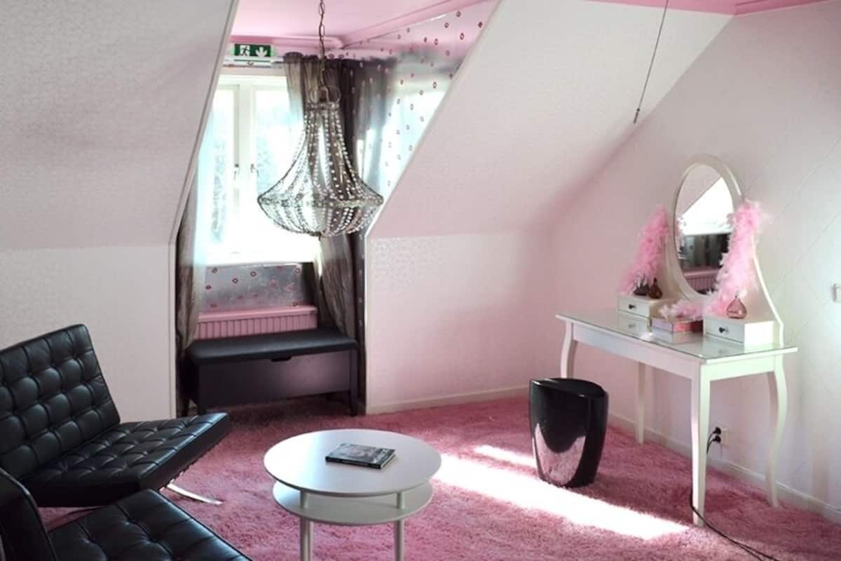 A room with a black leather sofa, a small round table, a white dresser with a mirror, and a hanging chandelier.