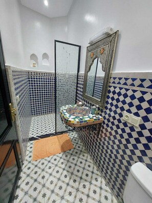 A bathroom with a tiled floor, a sink with a decorative mirror, and a shower area. - Riad Zaid (Marrakech)