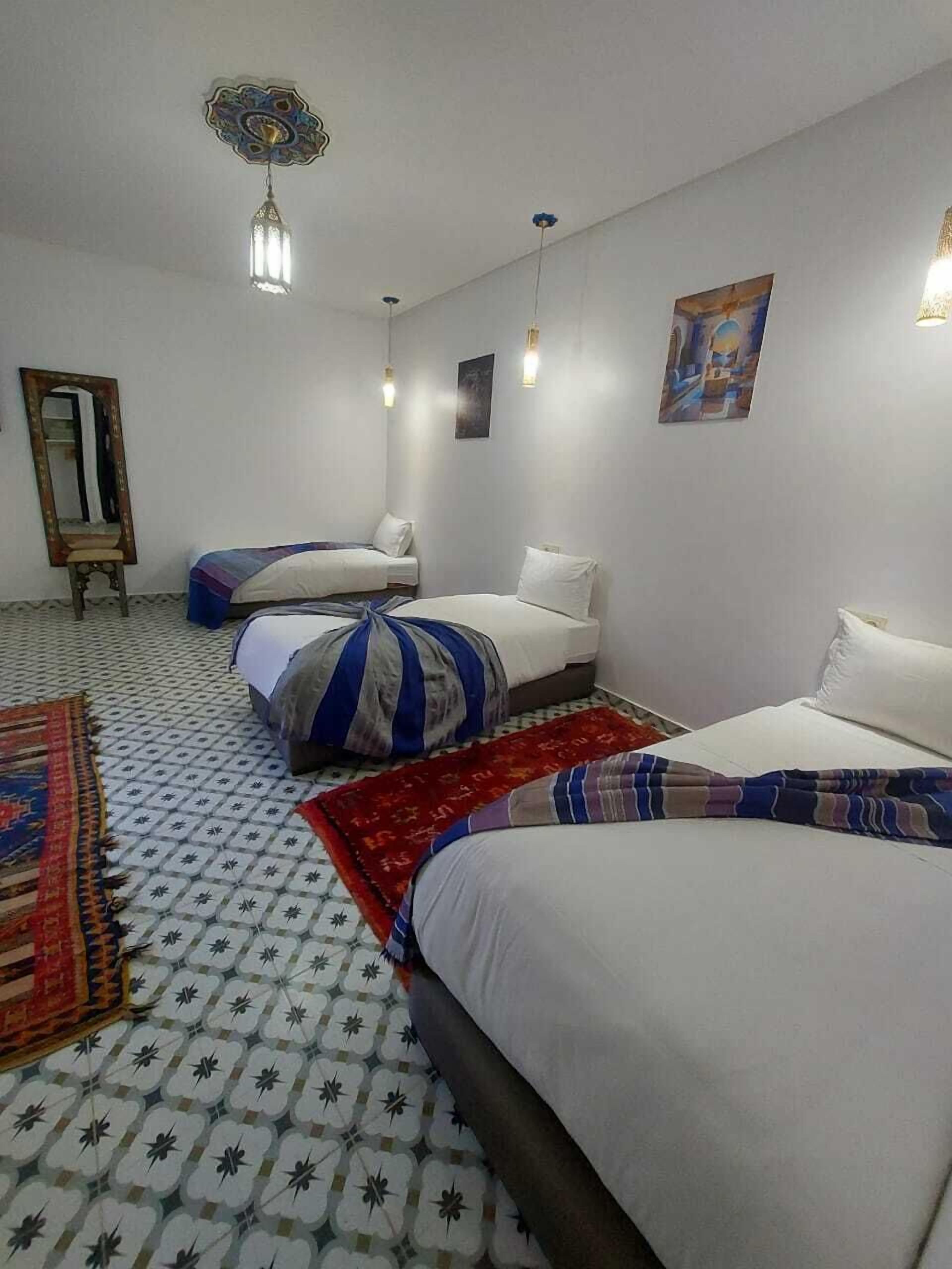 A hotel room with three beds, a mirror, and a painting on the wall.