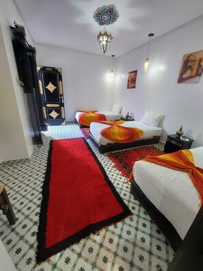 A hotel room with two beds, a red carpet, patterned floor, decorative ceiling light, and a black door with gold detailing. - Riad Zaid (Marrakech)
