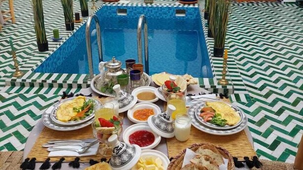 A dining table set with various dishes, a pool, and decorative elements in a room with patterned flooring and traditional decor. - Riad Zaid (Marrakech)