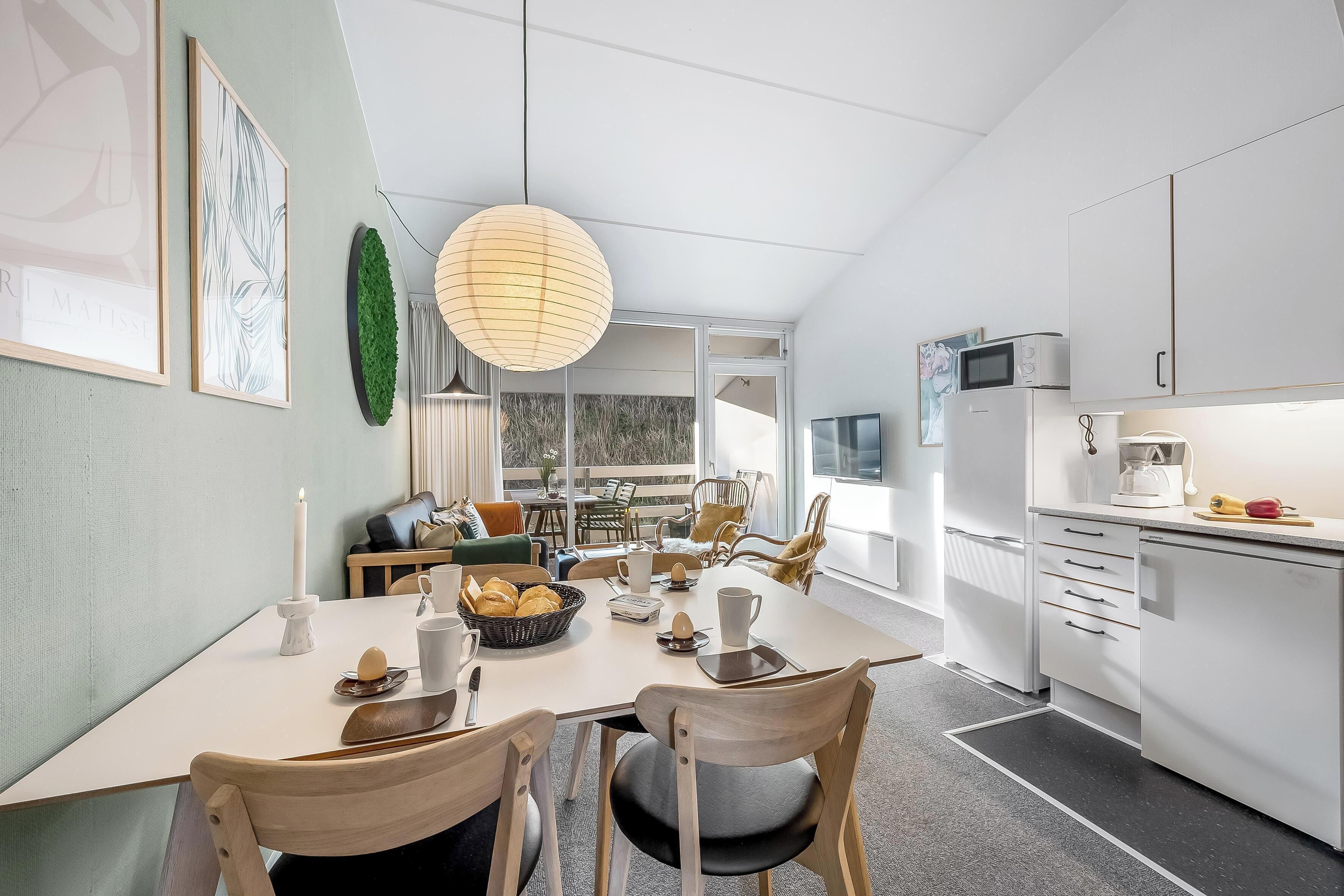 Een moderne keuken met witte kasten, een eettafel met stoelen en een groot raam dat natuurlijk licht binnenlaat.