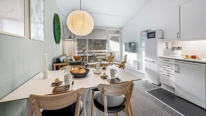 Et moderne køkken med hvide skabe, et spisebord med stole og et stort vindue der lukker naturligt lys ind.