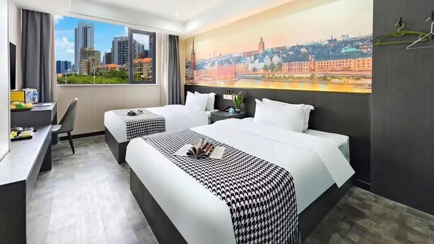 Habitación de hotel con dos camas, un escritorio y un ventanal con vista panorámica de la ciudad.
