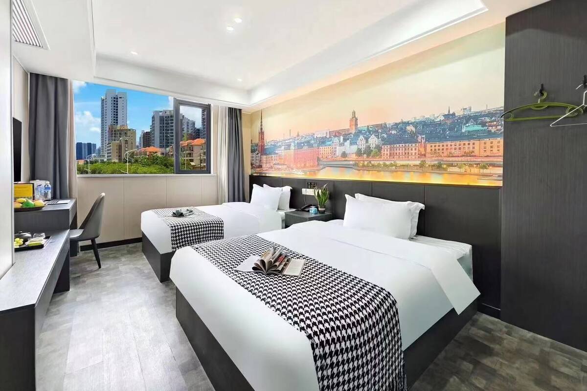 A hotel room with two beds, a desk, and a large window with a cityscape view.