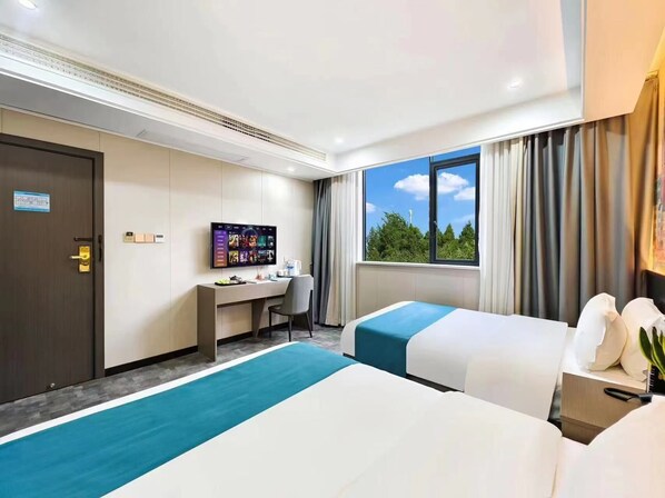 Een hotelkamer met twee bedden, een bureau, een televisie en een raam met uitzicht op bomen.