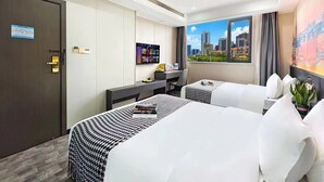 Habitación de hotel con dos camas, un escritorio y un ventanal con vista a la ciudad.