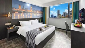 Habitación de hotel con una cama grande, un escritorio con una computadora portátil, vistas a un paisaje urbano y un cuadro de un puente famoso.