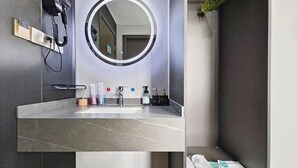 Un baño moderno con un lavamanos grande, un espejo redondo y un teléfono.